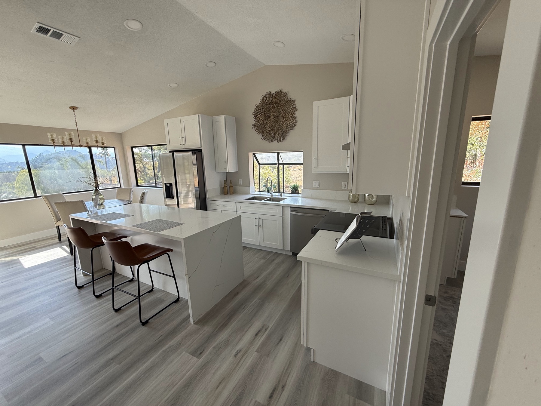 Finished open kitchen with a waterfall quartz island, white shaker cabinets and a vaulted ceiling